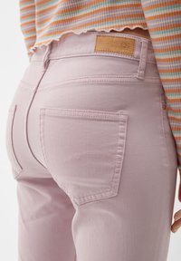 Personne portant un jean taille haute rose clair avec des poches arrière et un haut court à manches longues rayé aux tons orange, blanc et bleu.