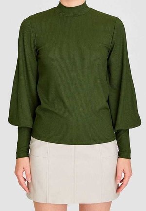 Persona que lleva una camiseta de manga larga con canalé en verde oliva con mangas abullonadas y cuello alto, combinada con una falda beige clara.
