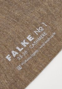 Brązowy kaszmirowy materiał z teksturowanym splotem, z białym nadrukiem "FALKE No 1 35-36 CASHMERE" oraz instrukcjami pielęgnacyjnymi na dole.
