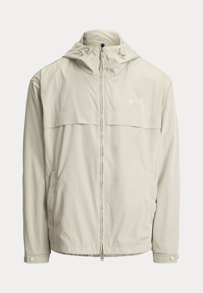 Veste à capuche beige clair avec fermeture éclair à l'avant, cordons ajustables sur la capuche, manches longues avec poignets à boutons-pression et poches latérales.