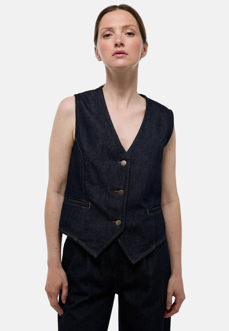 Gilet en denim foncé avec un col en V, trois boutons métalliques et poches avant. Présente des coutures contrastées et une coupe ajustée.