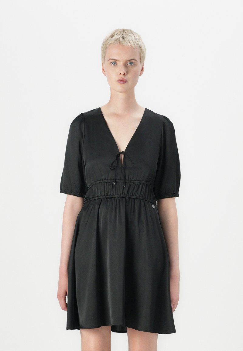 Vestido preto feito de tecido liso, com decote em V, laço frontal, mangas curtas bufantes e cintura elástica.