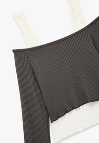 Ribbede crop top med off-white og mørkegrå sektioner, der har en boxy form og bred halsudskæring. Teksturert stof med rå kanter.