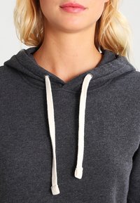 Sweat à capuche gris avec une texture en polaire, des accents à cordon de serrage crème, et une poche kangourou classique.