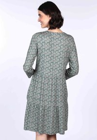 Grünes Blumendruckkleid mit langen Ärmeln, geraffter Taille und gestuftem Rock. Hergestellt aus weichem Stoff, mit rundem Ausschnitt und zartem Muster.