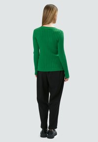 Maglione verde a coste con maniche lunghe e scollatura ampia, abbinato a pantaloni neri larghi e scarpe nere con suola spessa.