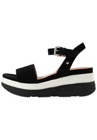 Sandalo in suede nero con una larga fascia, chiusura alla caviglia e una suola piatta a strati bianca e nera. Suola testurizzata per una migliore aderenza.