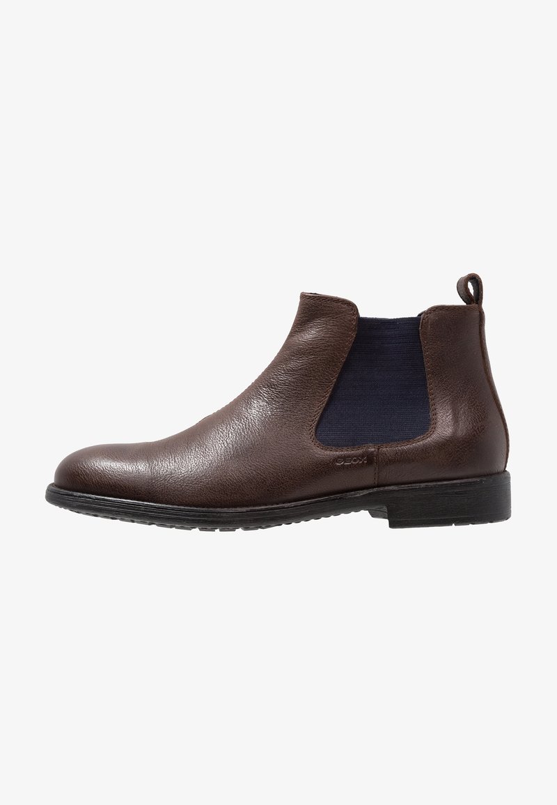 Bottine Chelsea en cuir marron avec panneau latéral élastique, semelle basse noire et languette à l'arrière.