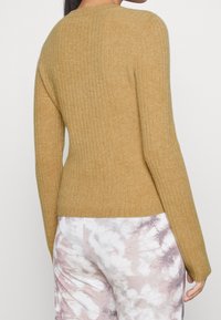 Maglione a coste giallo senape con silhouette aderente, scollatura rotonda e maniche lunghe, abbinato a pantaloni chiari con motivo tie-dye.