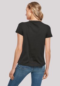 Black short-sleeve t-shirt with a rounded neckline and relaxed fit, paired with blue denim jeans, viewed from the back.