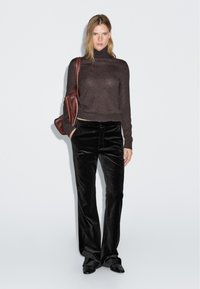 Mörkbrun polotröja kombinerad med svarta flared sammetsbyxor. Modellen bär en brun läderaxelväska. Mjuk textur överallt.