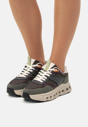 Zapatillas grises y moradas oscuras con cordones blancos, hechas de malla y materiales de cuero sintético. Suela gruesa de color crema con recortes. Etiqueta de acento verde.