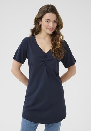 Tunique en V navy à manches courtes, avec des détails froncés au centre. Tissu lisse et coupe décontractée. Assorti à un jean bleu.