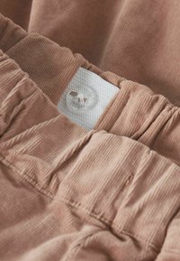 Beigen väristen samettihousujen joustava vyötärönauha, jossa sisäpuolella säädettävä nappi koon mukauttamiseksi.