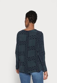 Maglietta a maniche lunghe blu navy con motivi geometrici, tra cui cerchi e quadrati. Tessuto morbido con una vestibilità rilassata. La vista posteriore mostra un collo arrotondato.