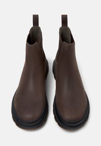 Bottines Chelsea en cuir marron avec une finition lisse, des panneaux élastiques sur les côtés, des languettes et une semelle en caoutchouc noir texturé.