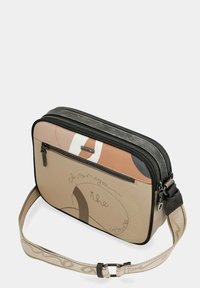 Prostokątna beżowa torba na ramię z zamykanymi na suwak przegródkami, abstrakcyjnym brązowo-białym wzorem oraz regulowanym paskiem ozdobionym logo marki.