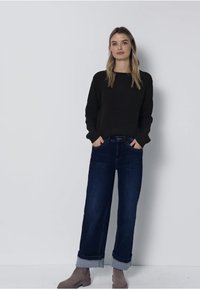 Tumma neulepusero, siniset leveälahkeiset farkut, joiden lahkeet on käännetty, ja taupemaiset nilkkurit. Yksinkertainen muotoilu, rento istuvuus ja yhtenäiset värit.