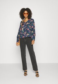 Blusa floral em azul-marinho com padrões coloridos, mangas longas e decote em V. Combinada com jeans pretos de perna reta e sandálias de salto pretas.