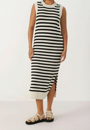 Robe sans manches en tricot avec des rayures noires et blanches, un col côtelé, une fente sur le côté et une coupe décontractée. Assortie à des sandales beiges.