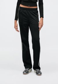 Čierne atletické nohavice s voľným strihom, vybavené bielymi bočnými pruhmi. Vyrobené z hladkej, ľahkej látky s elastickým pásom.