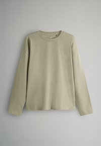 Beige Langarm-Shirt mit Rundhalsausschnitt in einfacher, lockerer Passform auf einem einfarbigen grauen Hintergrund präsentiert.