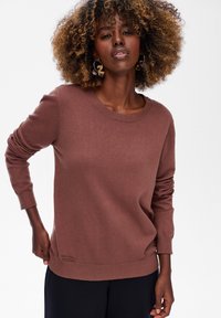 Brązowy sweter z dzianiny z okrągłym dekoltem, długimi rękawami i prążkowanymi mankietami. Posiada metkę z logo na dolnym lewym szwie.