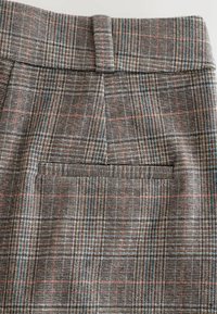 Wool-blend, gray plaid fabric with red and blue accents. Features a straight waistband and a single back pocket. Texture is slightly rough.