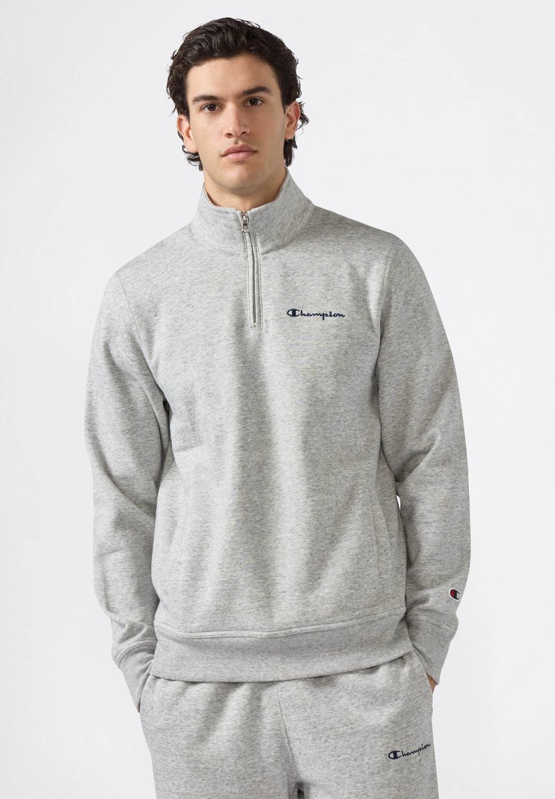 Felpa grigia con collo alto e chiusura a metà zip. Realizzata in un morbido tessuto con una sottile texture e logo ricamato sul petto.
