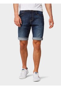 Tummansiniset farkkushortsit, joissa on haalistunut pinta, käärityt lahkeet, viisi taskua ja paksut tikkaus yksityiskohdat. Vaatteet yhdistetty valkoisiin lenkkareihin.