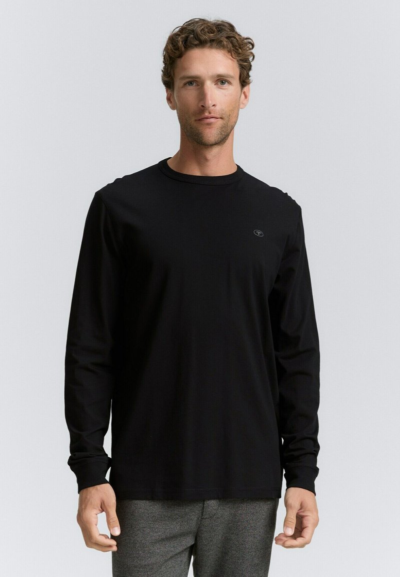 Zwarte lange mouwen shirt gemaakt van een gladde stof met een ronde hals; heeft een klein logo op de borst en aansluitende manchetten.