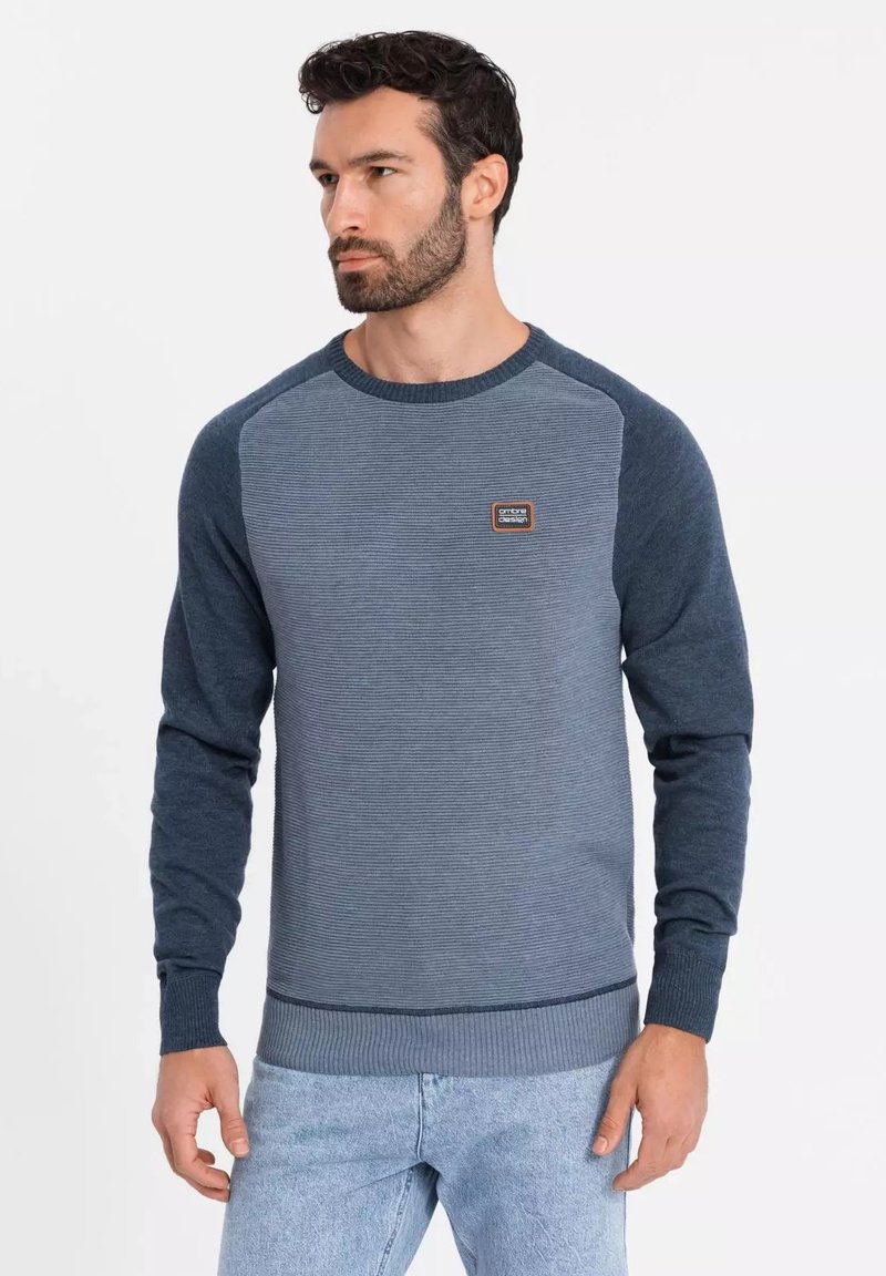 Suéter azul de cuello redondo con puños y dobladillo acanalados, patrón de rayas texturizado y un pequeño parche de logo en el pecho. Confeccionado con material suave.