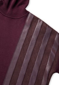 Bordowy sweter z golfem z naprzemiennymi pionowymi panelami z gładkiej skóry i zamszu na jednym rękawie.