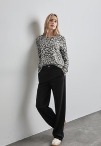 Camicia a maniche lunghe con stampa leopardata grigia abbinata a pantaloni larghi neri a vita alta e sneakers bianche, su uno sfondo neutro.