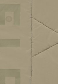 Beigefarbener gesteppter Stoff mit geometrischem Druck in matter Optik. Die Nähte bilden dreieckige Muster, die Textur hinzufügen.