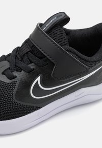 Baskets de sport noires avec dessus en maille, accents moulés et bande Velcro. Équipées d'un logo swoosh blanc et d'une semelle rembourrée.