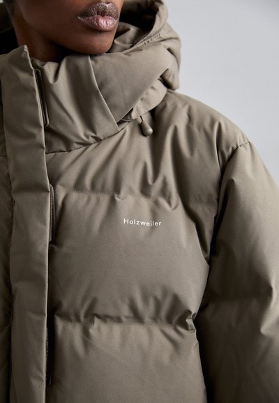 Beige puffjacka med hög krage, horisontell sömnad och en vit logo. Materialet är slätt och lite glansigt.