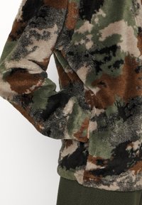 Fuzzy pullover i camouflage mønster med nuancer af grøn, brun og sort. Blød tekstur med rund halsudskæring og lange ærmer.