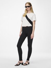 Hvit forkortet t-skjorte, svarte leggings og svarte hæl-sandaler. Modellen har på seg svarte solbriller med et strømlinjeformet design. Enkel, moderne estetikk.