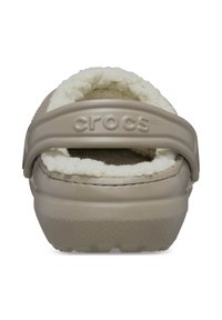 Beżowe klapki Crocs z białym futrzanym wykończeniem i paskiem piętowym z wytłoczonym logo "crocs", widok z tyłu.