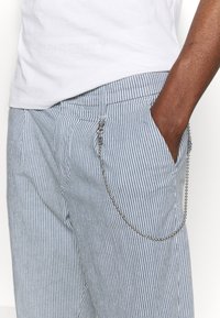 Striped blue and white trousers featuring a metal chain attached at the pocket. Material appears smooth with a tailored fit and flat front.