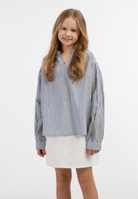 Stribet langærmet skjorte i blå og hvid, med v-hals, afslappet pasform og opsmøget ærmer, parret med en hvid denimnederdel.