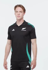 Polo noir avec des accents turquoise, présentant des manches courtes, un col et un logo brodé sur la poitrine. Décoré de trois rayures.