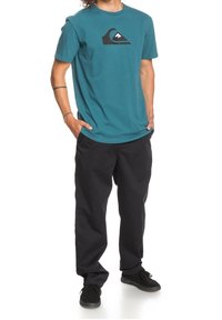 Tyrkysové bavlněné tričko s černým logem, doplněné černými kalhotami. Oblečení má volný střih, krátké rukávy a kapsy. Černé tenisky dokončují vzhled.