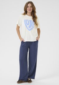 T-shirt crème avec un graphique de cœur bleu, assorti à un pantalon marine ample. Tissu doux et coupe décontractée, avec des poches sur les côtés. Chaussures décontractées.