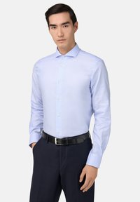 Lichtblauw blouse met lange mouwen en een gestructureerde kraag, verticale strepen en knoopsluiting; gedragen met donkere broeken en een zwarte riem.