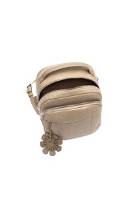 Béžová kožená crossbody taška s dvojitým zipsom, zaobleným tvarom a kvetinovým príveskom. Hladký povrch a nastaviteľný popruh pre pohodlné používanie.