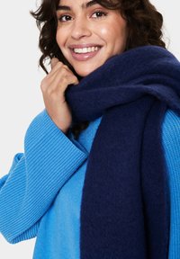 Blue ribbed knit sweater paired with a soft, dark navy scarf, featuring a snug texture, worn around the neck, highlighting the cozy appearance.
