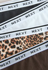 Fyra par underkläder i olika färger: svart, vit, brun och ett leopardmönster, alla med vita band märkta "NEXT."