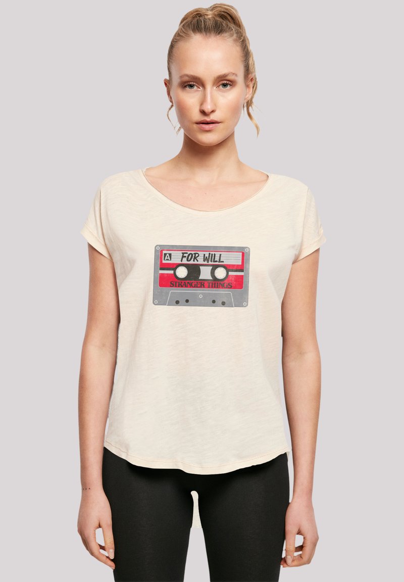 Cream-colored T-shirt with a relaxed fit, featuring a graphic of a cassette tape with red and black details and the text "FOR WILL STRANGER THINGS."